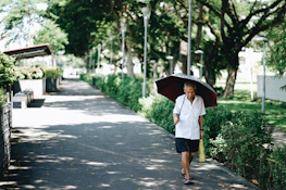 An older adult smiling while walking in a peaceful park surrounded by lush greenery.