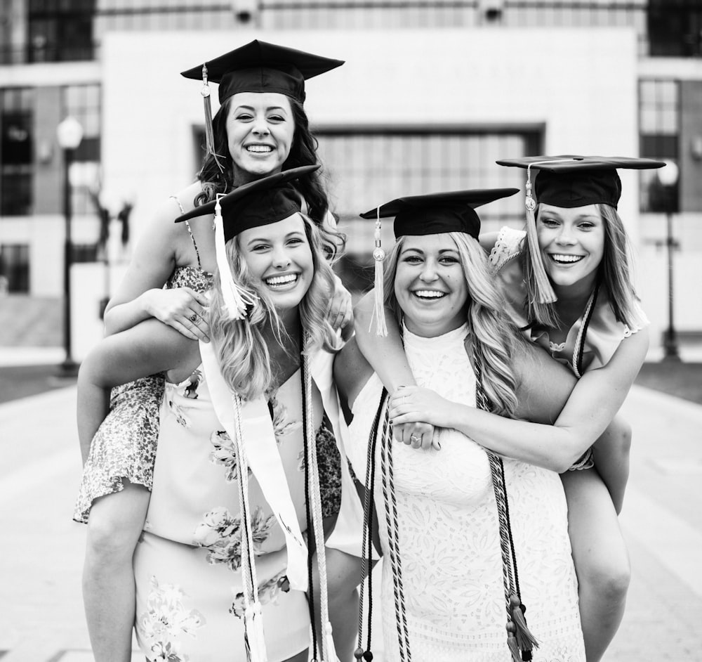 A group of girls wearing graduation caps smiling happily in front of their school