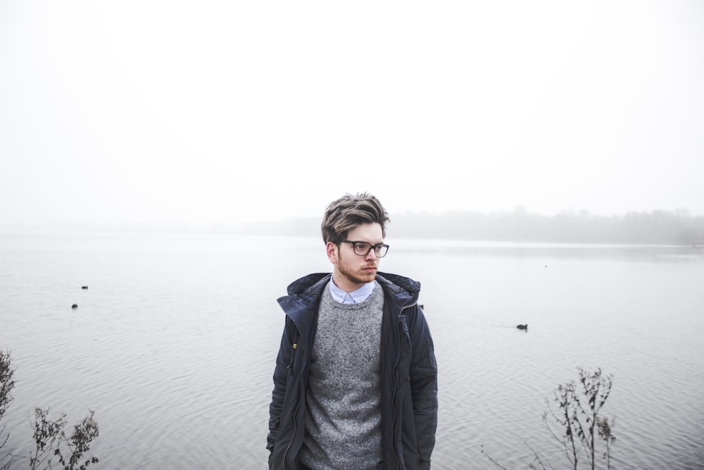 man wearing black jacket standing near body of water