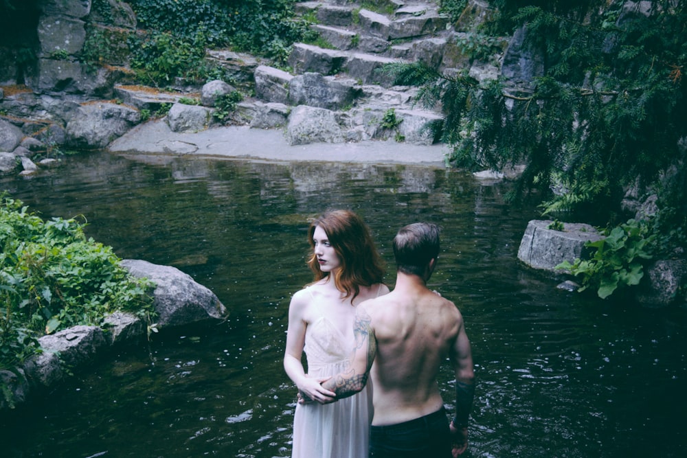 homem e mulher em pé no corpo de água ao lado de árvores de folhas verdes