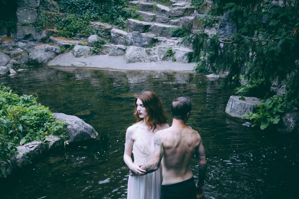 man and woman standing on body of water beside green leafed trees