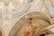An intricately decorated ceiling features detailed artwork and patterns. The design includes ornate carvings, geometric shapes, and classical figures. The color palette comprises gold, beige, and black accents, lending a luxurious and historic feel.