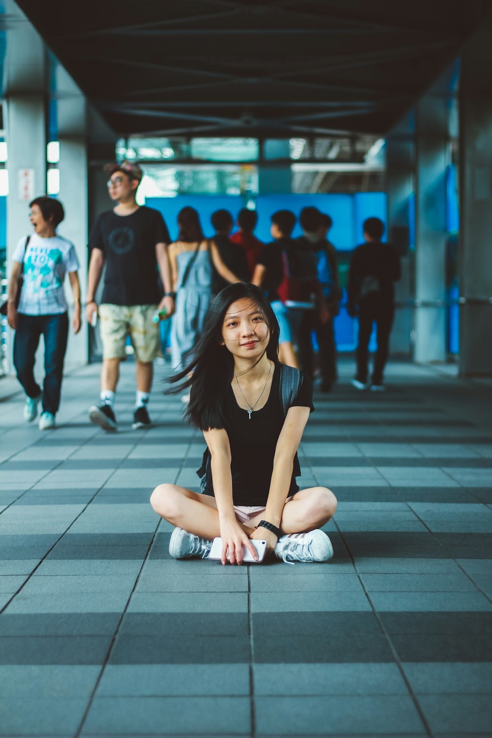 woman carrying backpack while sitting cross legs on hallway in front of people walking