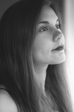 A black and white portrait of a woman gazing thoughtfully out of the frame. Her expression is serene, and her long hair is smooth and flowing over her shoulders. The lighting creates a soft, gentle contrast emphasizing her features.
