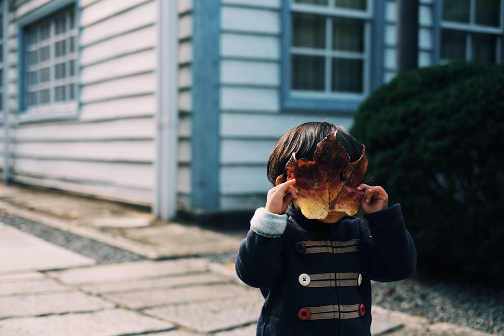 niño pequeño cubriendo su cara con una hoja