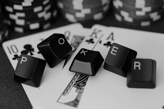 A series of playing cards and poker chips are displayed. The cards, including a ten, jack, queen, king, and ace of clubs, are spread out with black keyboard keys arranged to spell the word 'POKER'. The image is in black and white, giving it a classic, stylish look.