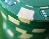 A close-up view of a stack of green poker chips with white accents and indented designs around the edges.