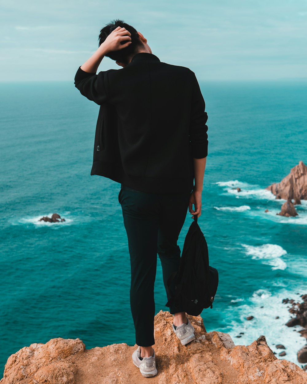 man standing on top of mountain facing backwards at body of water