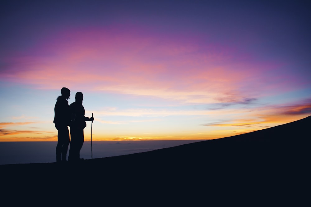 silueta de dos hombres que caminan en la cima de la montaña