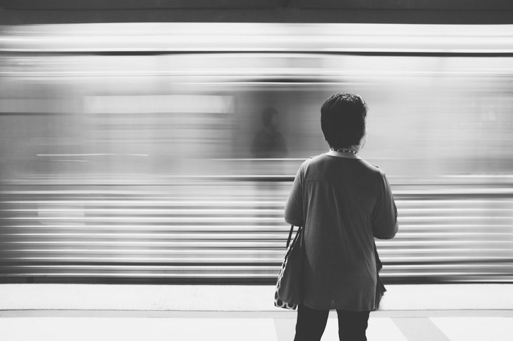 grayscale photography of woman standing near train