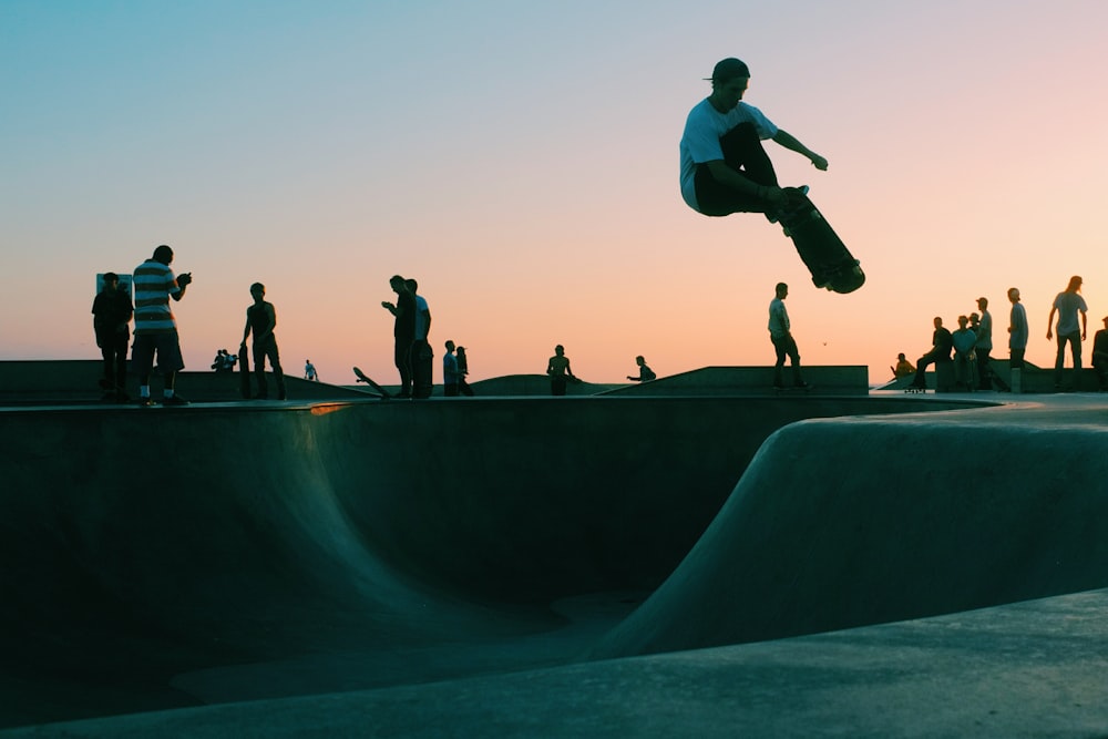 Uomo che fa il trucco al parco dello skateboard durante il tramonto