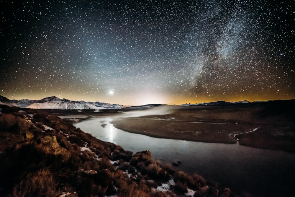 river surrounded by brown grass field under star sky