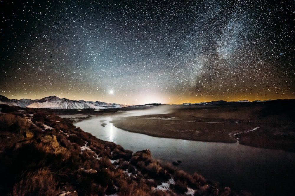 río rodeado de campo de hierba marrón bajo el cielo estrellado