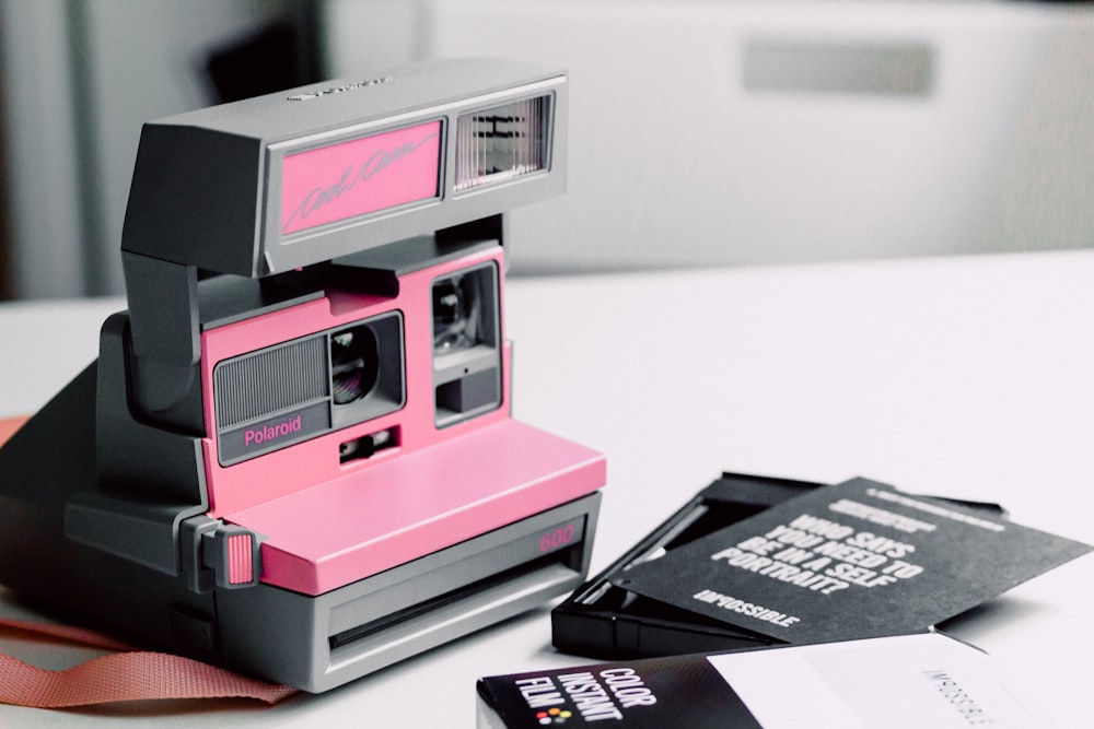 Fotocamera istantanea Polaroid rosa e grigia su superficie in legno bianco