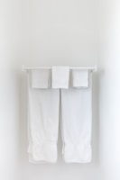 Two neatly folded white towels hang from a clean, white towel rack against a plain, light-colored wall.