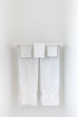 Two neatly folded white towels hang from a clean, white towel rack against a plain, light-colored wall.