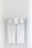 Two neatly folded white towels hang from a clean, white towel rack against a plain, light-colored wall.