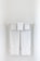 Two neatly folded white towels hang from a clean, white towel rack against a plain, light-colored wall.
