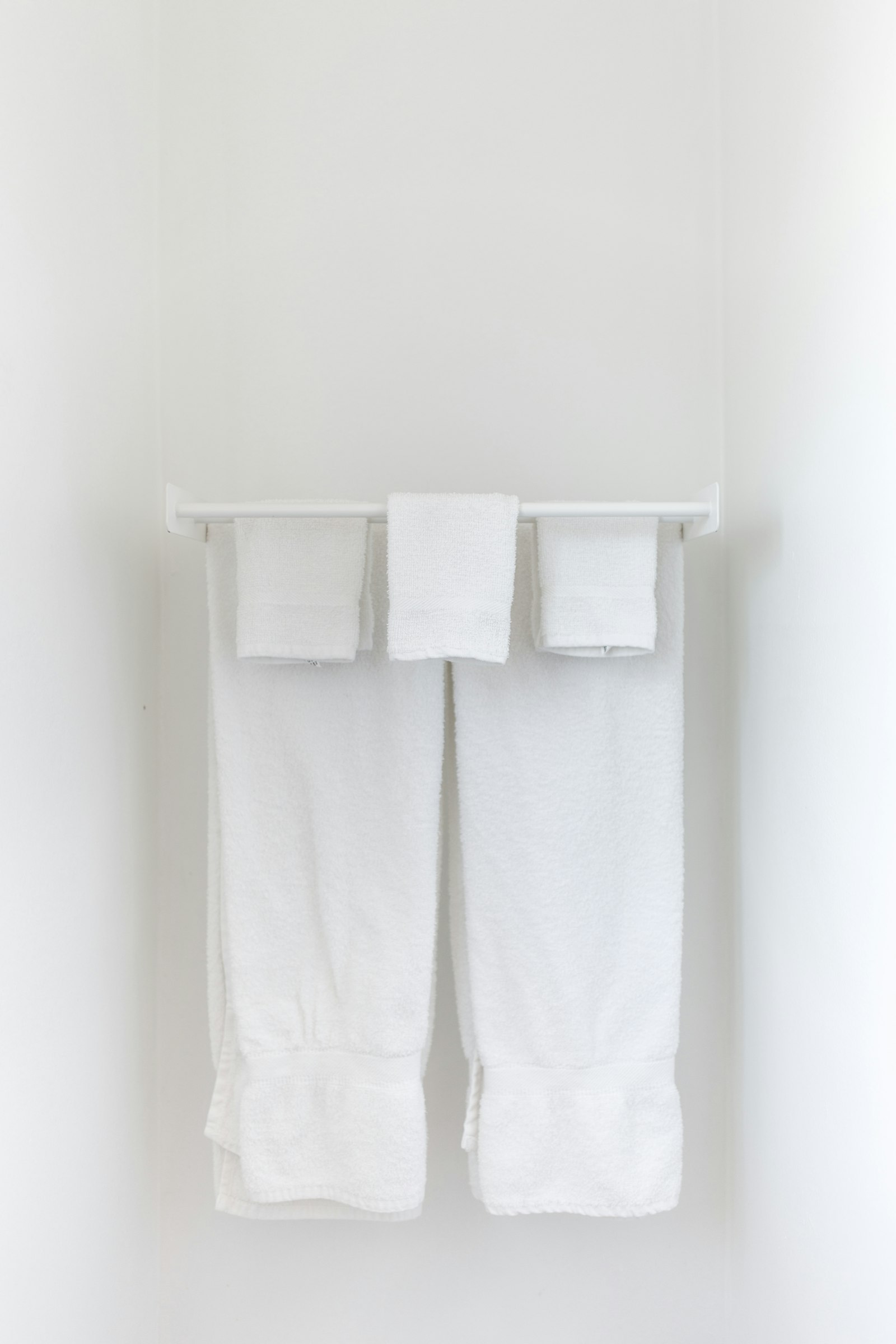 White towels folded over a towel bar on a bright white wall