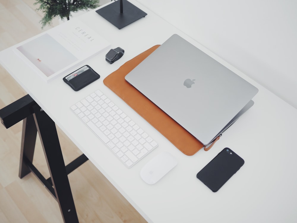 MacBook argenté et téléphone sur table blanche