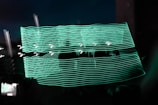 A dark background with bright, wavy lines of neon green light creating an abstract pattern. These lines are superimposed over a shadowy figure or object, giving a sense of motion or dynamic energy.
