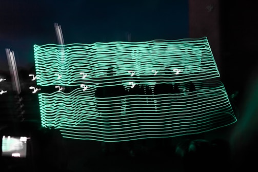 A dark background with bright, wavy lines of neon green light creating an abstract pattern. These lines are superimposed over a shadowy figure or object, giving a sense of motion or dynamic energy.