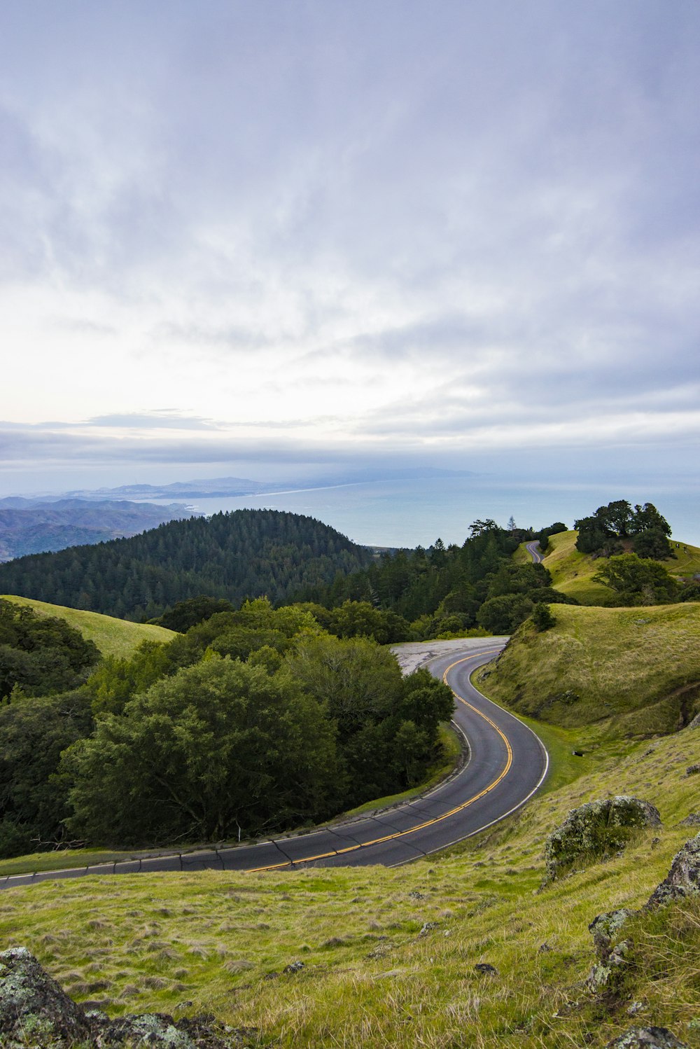 Curva strada asfaltata su collina vicino al mare sotto cielo nuvoloso