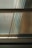An abstract composition of light and shadows is visible through textured glass. The sunlight filters through, casting soft, elongated shadows, creating an interplay of patterns on the surface. Horizontal lines of metal frames divide the glass, contributing to a minimalist yet dynamic appearance.