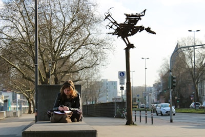 A young woman sitting on a bench, writing in a notebook.
