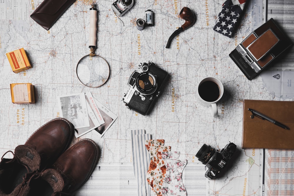 macchina fotografica, paio di scarpe marroni, tazza in ceramica bianca, penna grigia e nera, pipa da fumo marrone