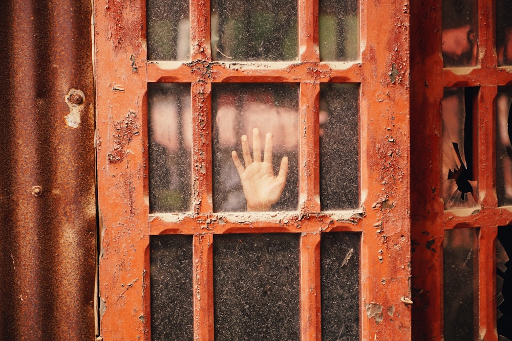person hand on glass panel door with red wooden frame