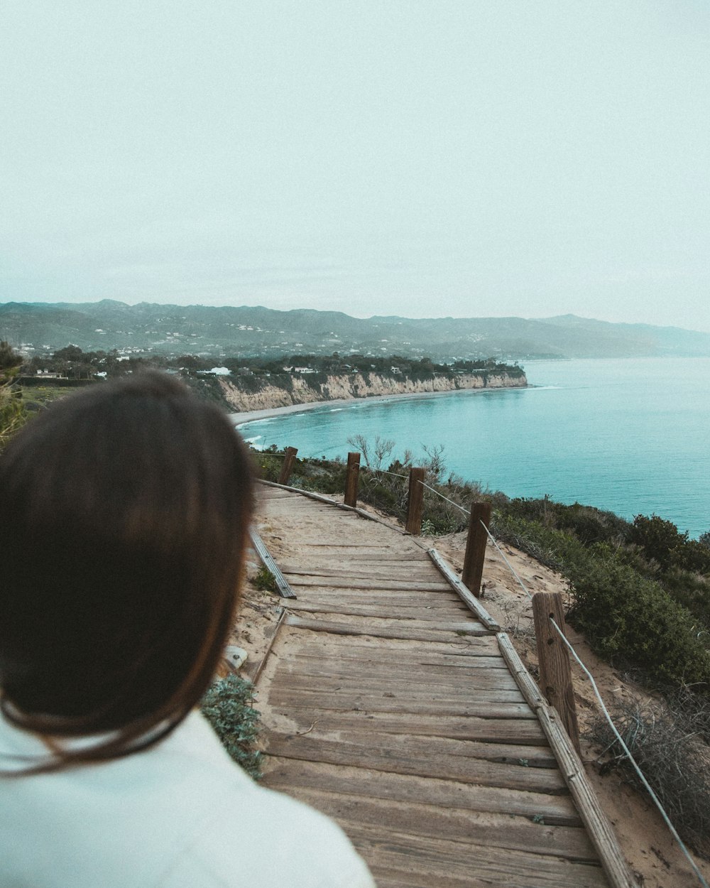 a woman walking down a wooden walkway next to a body of water