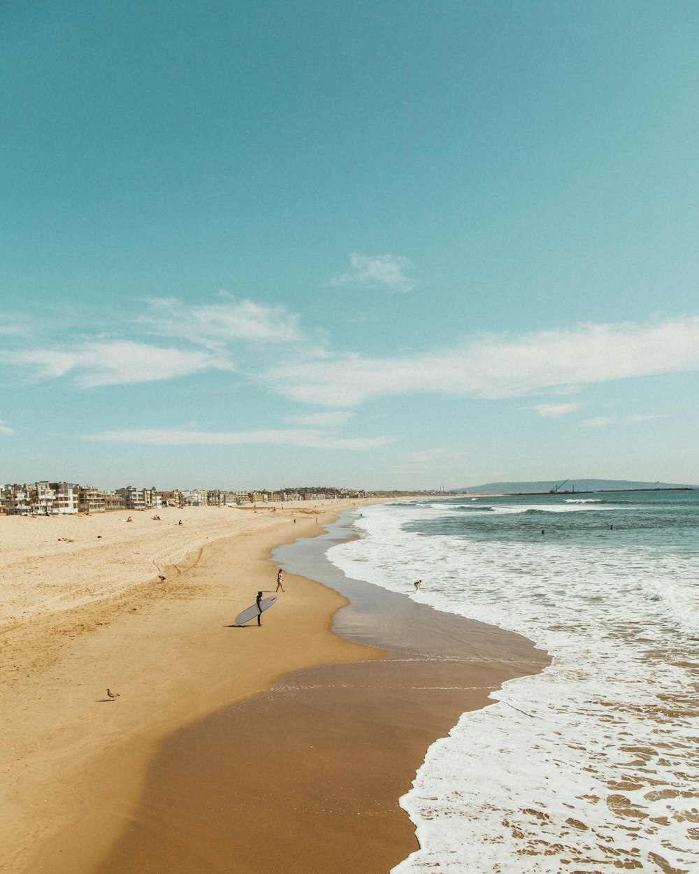 hombre de pie mientras sostiene una tabla de surf mirando hacia la orilla del mar