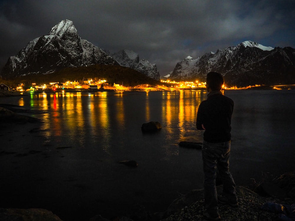 man standing near body of water far away from building during nighttime