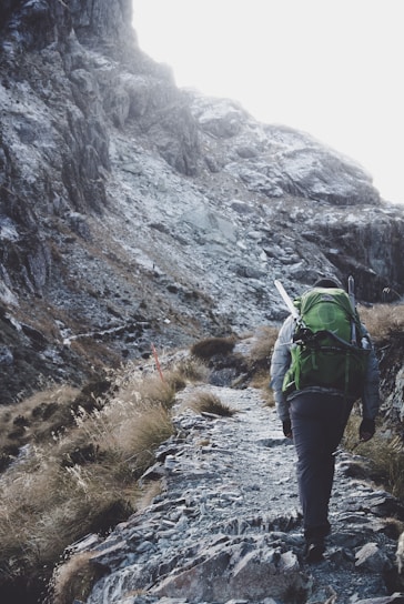 A climber ascending a rugged mountain trail with sturdy gear from anmalds llc.