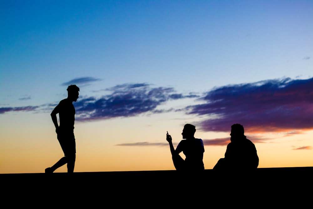 silhouette of three persons under blue and orange skies