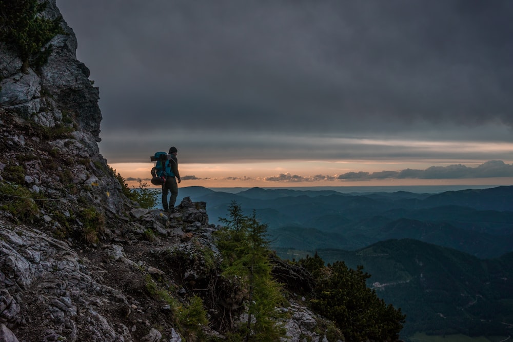 Persona de pie cerca del acantilado con vista de las montañas bajo las nubes de nimbo