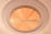 A close-up view of a round Harman Kardon speaker or audio component with a golden metallic finish, embedded in a circular frame. The texture and sheen of the material are visible, highlighting its premium build.