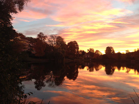 A cozy lakeside home at sunset with vibrant autumn trees reflecting on the water.