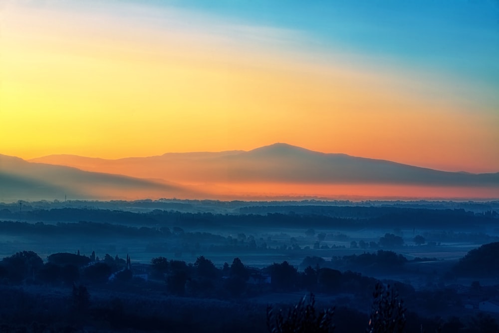 オレンジ色の夕暮れ時の山の近くの木々の風景写真