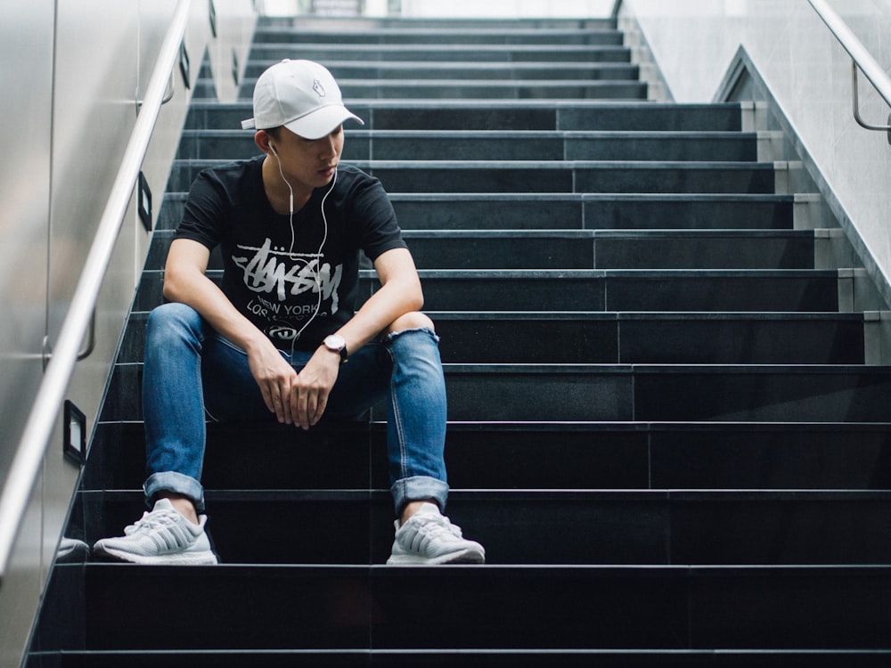 man sitting on black staircase while listening