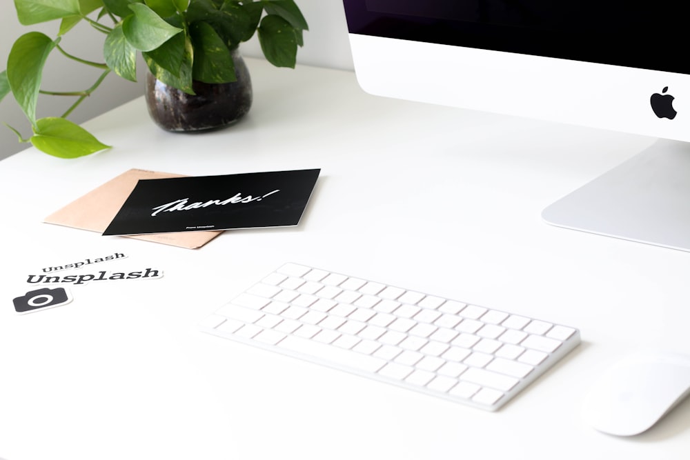 A Mac computer, keyboard and mouse on a desk with a plant.