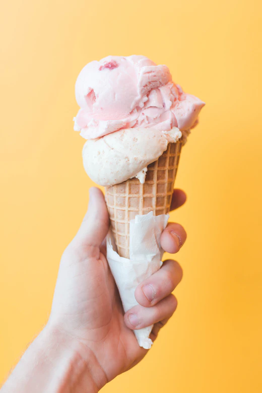 Bright creamy citrus gelato cone held up on a yellow background