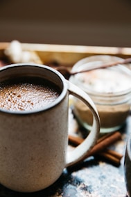 beige mug with hot chocolate near cinnamon sticks on surface