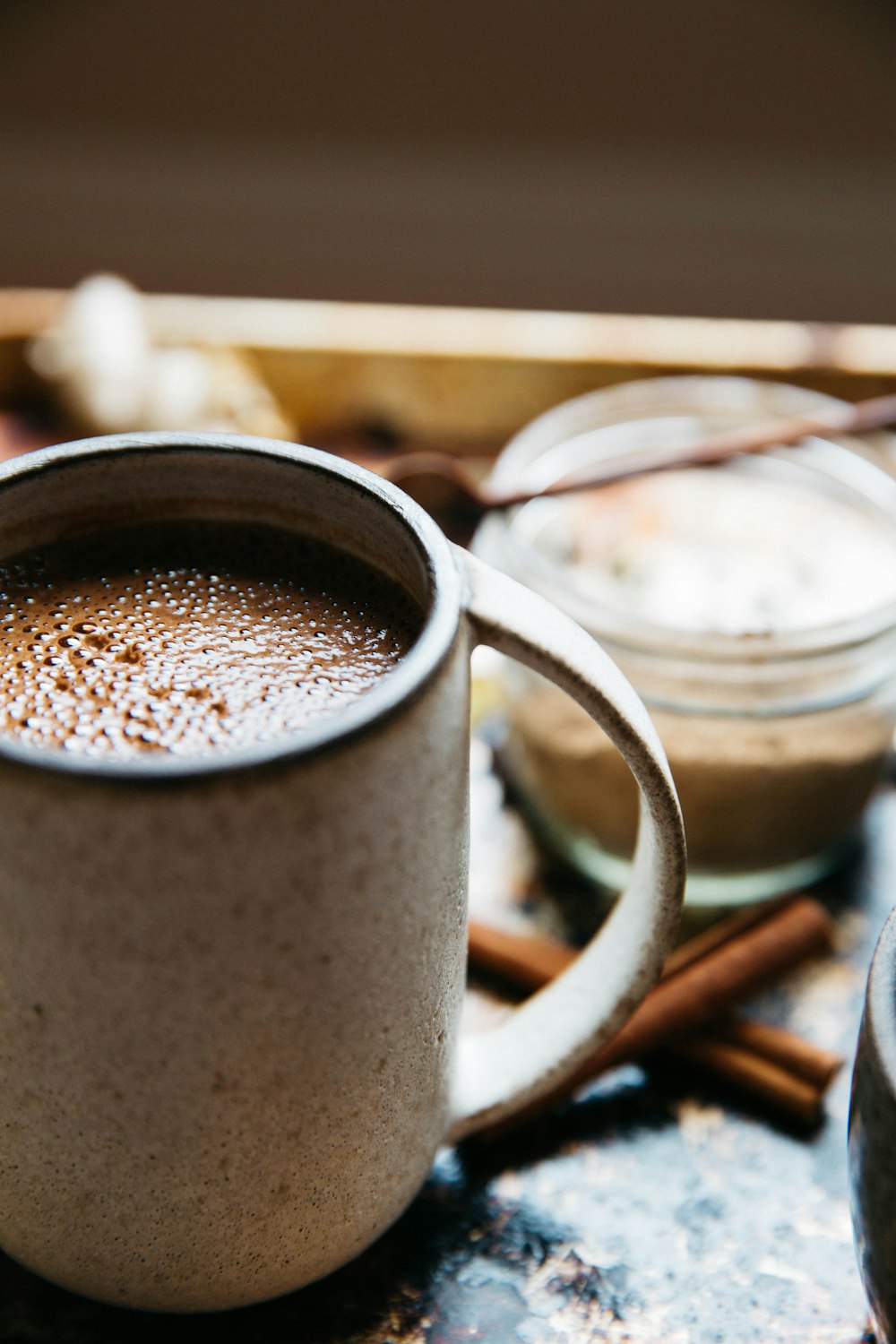 beige mug with hot chocolate near cinnamon sticks on surface