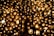 A multitude of glowing circular lamps are clustered together, creating a warm, golden ambiance. The lamps are arranged in a dense pattern with a lattice-like structure running vertically through the center. The light emitted is soft and diffused, casting a serene glow across the scene.
