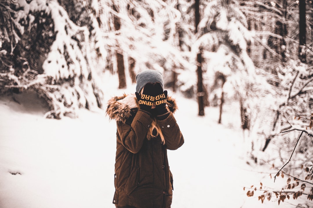 person standing on snow field surrounded by trees covering his face with his hands