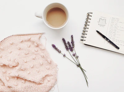 Digital tablet displaying a knitting pattern PDF surrounded by soft pink and white yarn.