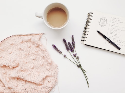 A cozy, softly lit workspace with pastel yarns, knitting needles, and a steaming cup of tea by a window.