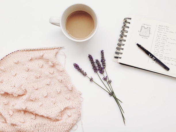 A cozy corner with a journal, knitting needles, and a small vase of fresh flowers on a wooden table.